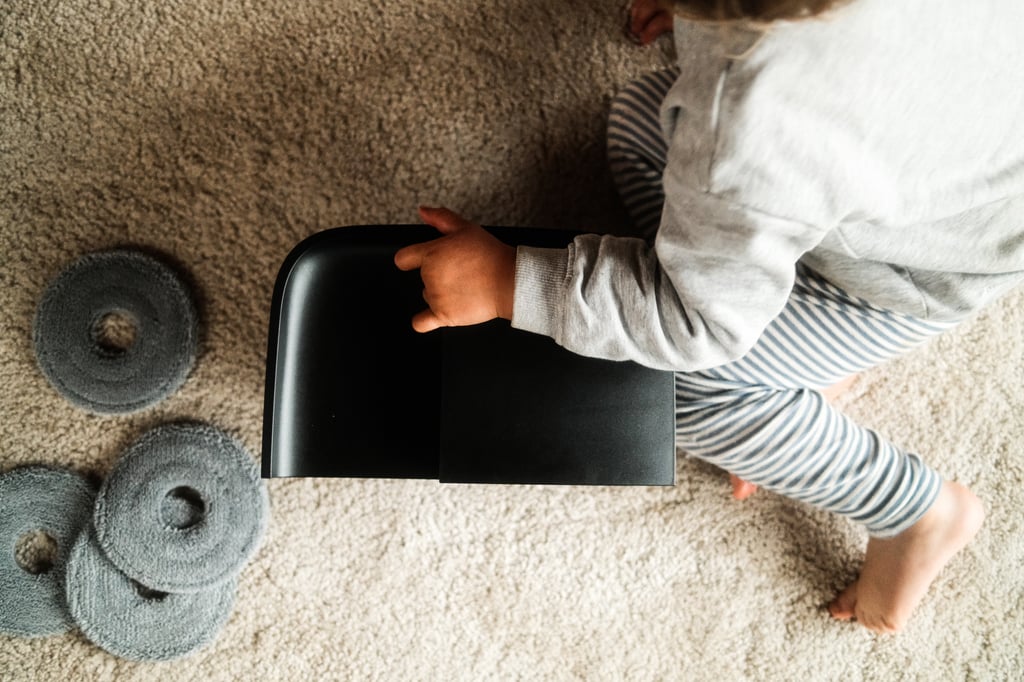 En toåring holder på den svarte vanntanken ved siden av flere grå ekstra moppeputer på teppet