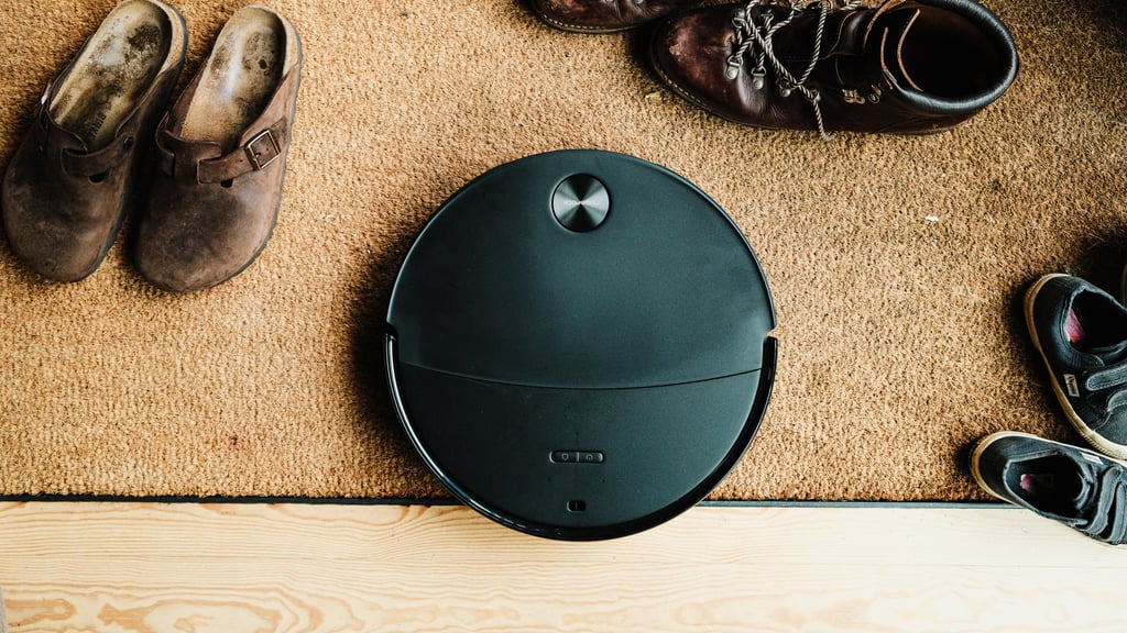 Roborock Saros 20 Neo sett ovenfra på en kokosmatte med sko, ved kanten mot tregulvet