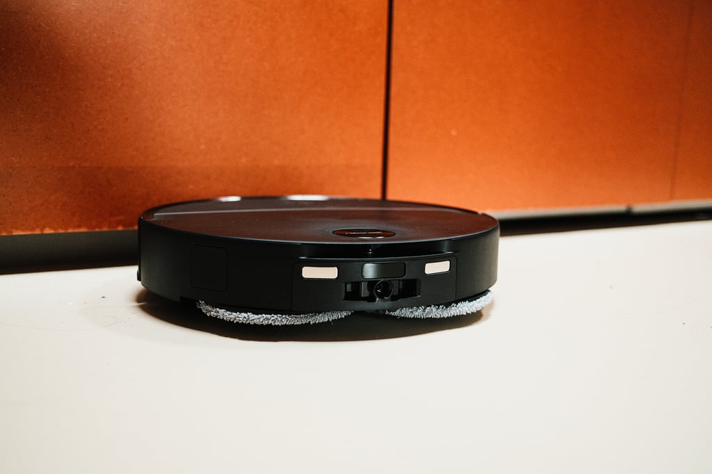 Roborock Saros 20 Neo sett fra siden foran en oransje skapvegg, med de to moppeputene synlige under