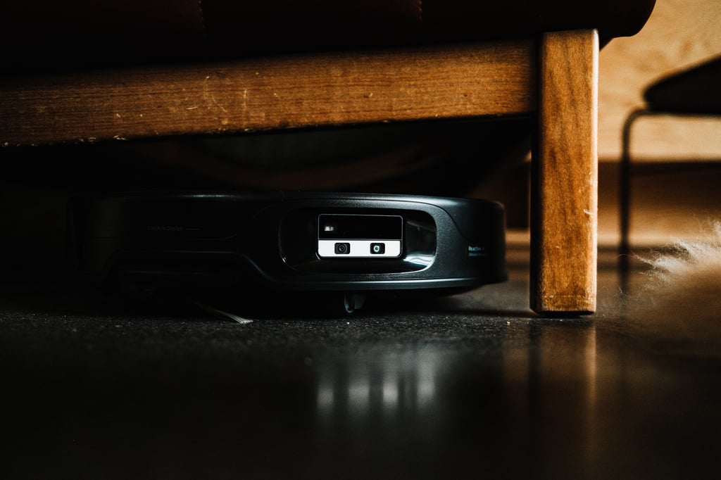 Roborock Saros 20 Neo kjører inn under en sofa med trebein, fotografert fra gulvhøyde