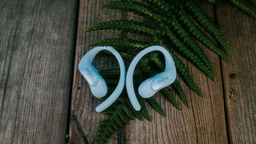 To isblå Shokz OpenFit Air 2-propper på et terrassebord med en bregne under