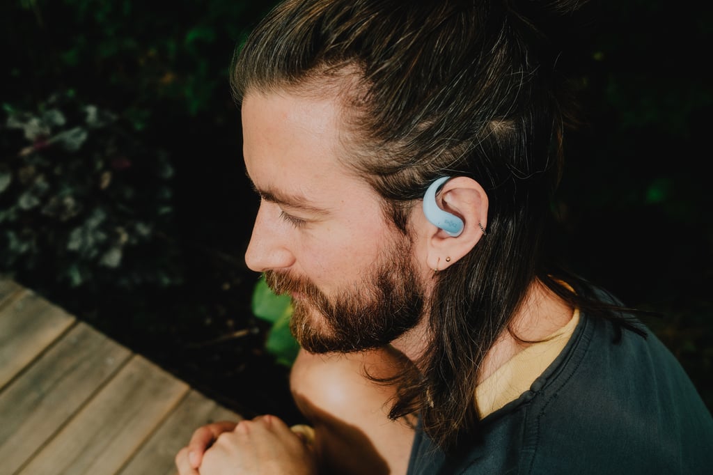 Julian med en isblå Shokz OpenFit Air 2 på øret, sett fra siden