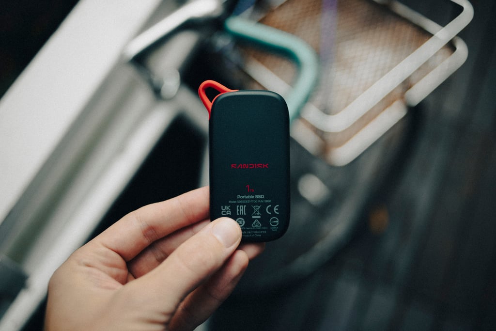 Baksiden av Sandisk Portable SSD holdt i hånden, med merkingen Portable SSD og sertifiseringsmerker