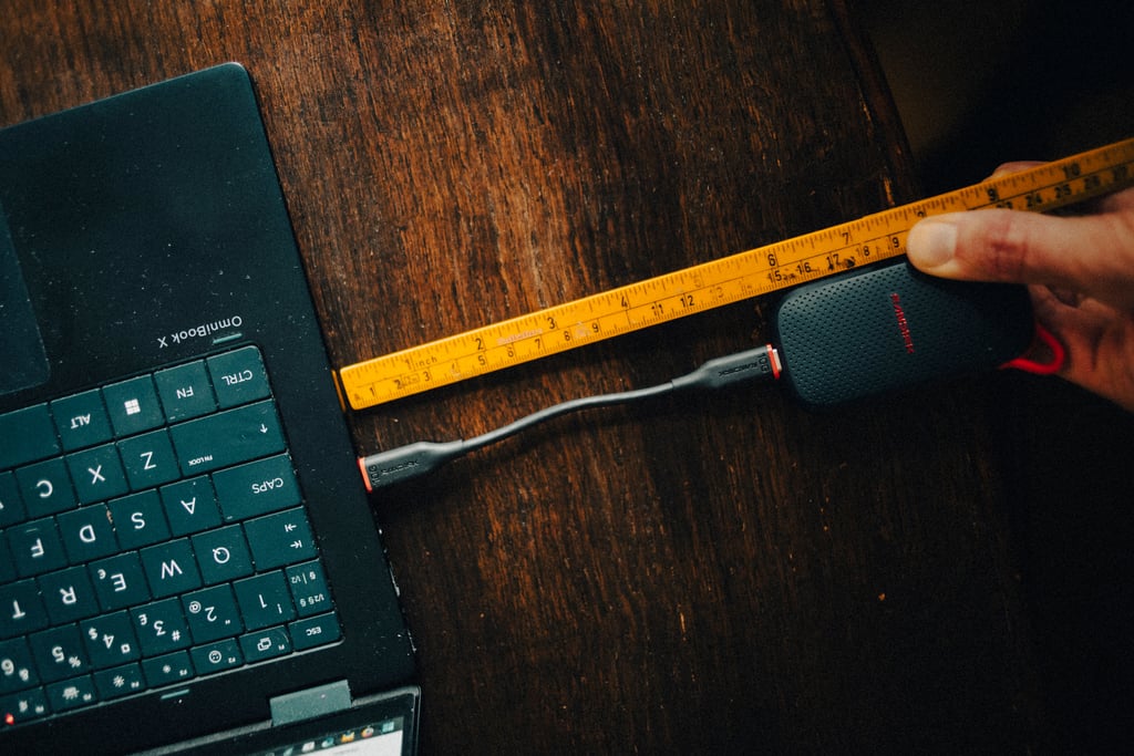 Den korte USB-C-kabelen kobler Sandisk Portable SSD til en laptop, med en tommestokk ved siden av