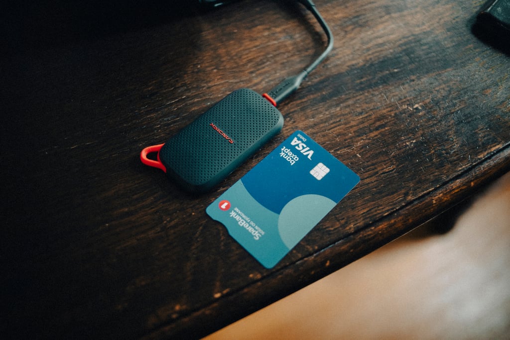Sandisk Portable SSD med kabel ligger ved siden av et bankkort på et mørkt trebord