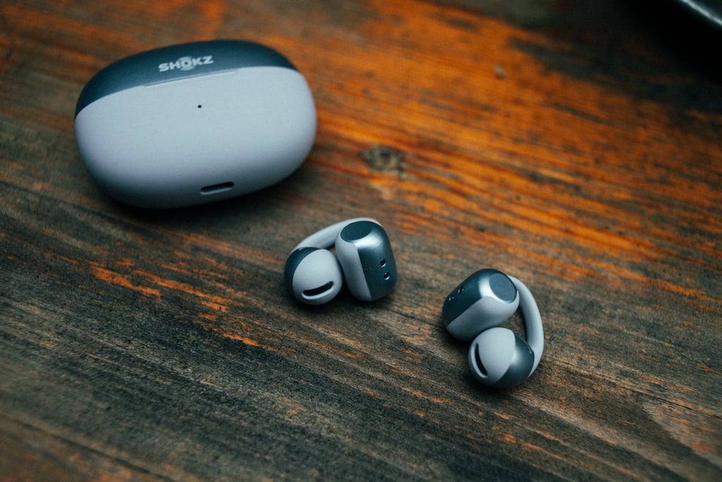 Ladeetuiet og begge proppene til Shokz OpenDots 2 liggende på et slitt trebord