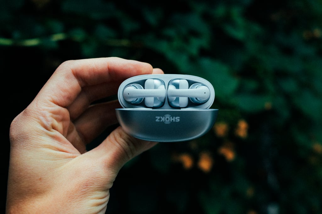 Ladeetuiet til Shokz OpenDots 2 holdt opp i en hånd med begge proppene synlige