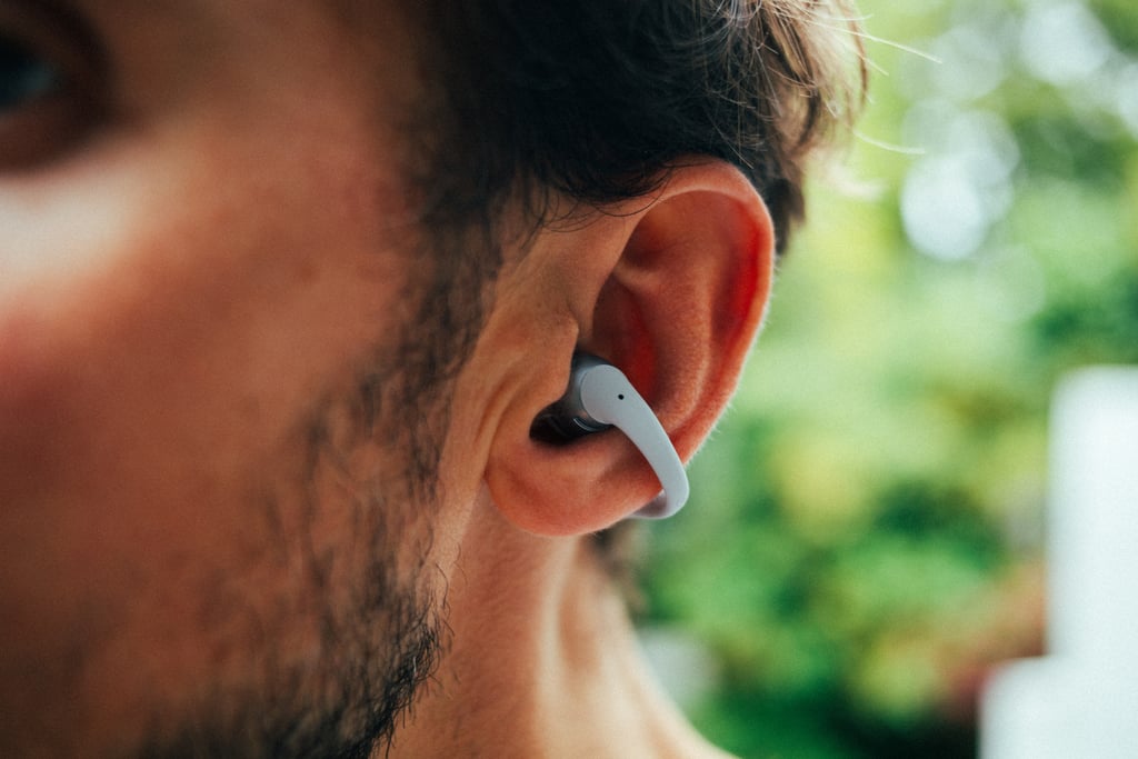 Shokz OpenDots 2 sitter klemt om ørekanten på en mann, sett i profil utendørs